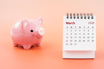 Desk calendar for March 2026 and pink piggy bank.