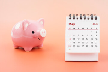 Desk calendar for May 2026 and pink piggy bank.