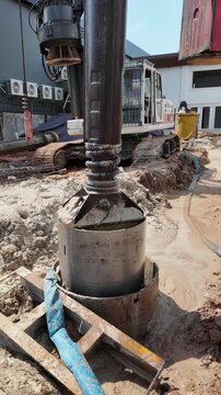 close up of a bored piling drilling bucket being lowered into a borehole at a muddy construction site.