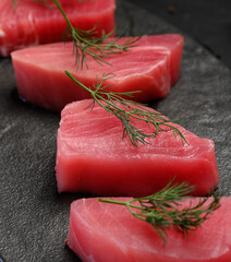 Raw tuna pieces on a black board, decorated with dill sprigs