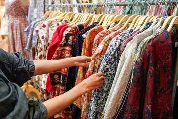 Close up of woman hand choosing discount colorful t-shirt clothes in store, searching or buying cheap cotton shirt on rack hanger at market ,stall shopping apparel fashion concept.