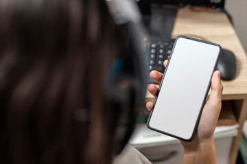 Unrecognizable female teen wearing headphones holding a smartphone turned on with white blank screen