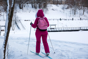 Woman in pink sportswear skiing in winter park. Skier walking by snow