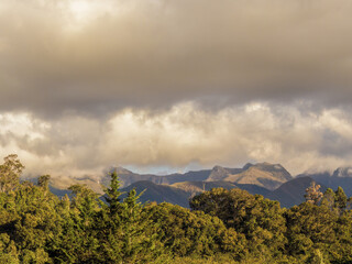 Fototapeta premium The Iguaque natural reserve behind the forest illuminated by the light of sunset, under an overcast sky, at the eastern Andean mountains of central Colombia.