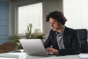 Fotobehang Sportwinkel Young businessman typing on laptop at desk in modern office, natural light with plant background, concept of productivity, focus, and business success  © ImageFlow