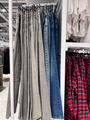 Jeans, shirts, and other clothes are hanging on hangers in the store.
