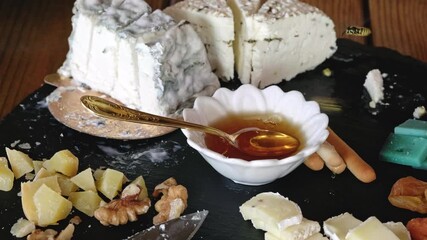 An artful arrangement of cheeses, honey, and nuts sits on a dark slate platter. Cubed cheese, dried apricots, and bread sticks enhance the display