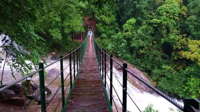 Young woman standing on a suspension bridge above Bambarakiri Ella in Sri Lanka. Female traveler enjoying nature, adventure travel and tropical landscape, freedom and exploration concept.