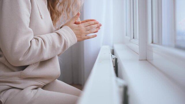 silhouette frozen woman warms hands on warm radiator. person hand touching cold heater. low temperature cold winter. Saving utility bills. Expensive inefficient central heating. girl in warm clothing