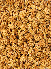 top view of shelled walnut halves scattered across a light pink textured background. The composition is minimalistic, with most walnuts gathered in the lower part of the frame, creating a natural, org