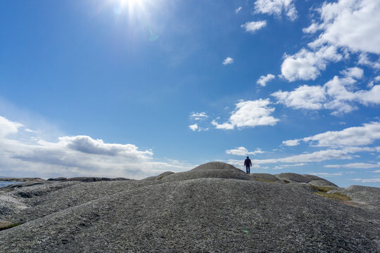 Person Standing on Smooth Rocky Landscape at Verdens Ende Norway under Sunny Blue Sky