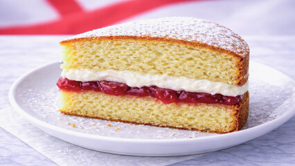 Classic British Victoria sponge cake slice with soft crumb, cream filling and red jam, served on white plate.