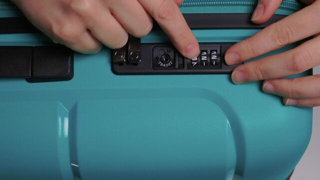 Secure suitcase with combo lock, Hands set combination on teal suitcase with textured surface, Closeup of hands adjusting numeric lock on stylish teal travel suitcase