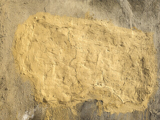 Weathered wall displays a patch of yellow plaster, showcasing cracks and rough texture. Bright daylight emphasizes the worn appearance of the outdoor setting.