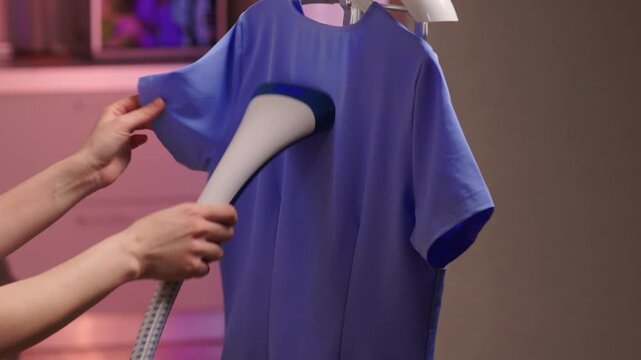 Blue shirt steaming, Blue uniform hanging while expertly steamed for wrinkle removal, Navy blue outfit on hanger being carefully steamed to remove creases professionally