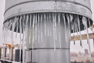 Metal vent with hanging icicles, Frozen icicles draping metallic chimney vent, Closeup of icy metal...