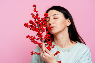 Woman holding red berries, eyes closed, feeling calmness against pink background
