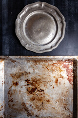Used oven flat baking pan with burned spots and scratches and pewter plate on black chalkboard background