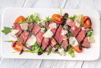 Italian beef tagliata salad with arugula and balsamic glaze on white plate