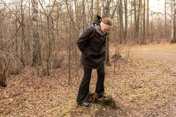 Naklejka premium Young woman standing on a tree stump in an autumn forest, looking down at the ground. Nature exploration and discovery concept for outdoor activity.