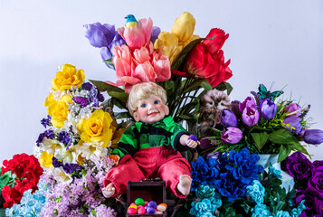young boy doll sitting on chair in bare feet holding jelly beans in front of spring flowers with white background