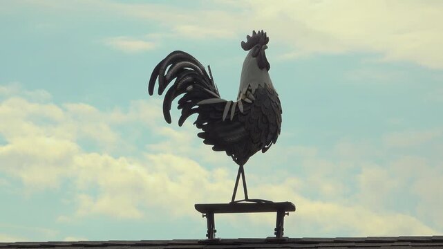A decorative rooster weather vane stands atop a roof against a blue sky. Rustic farm charm evokes countryside mornings, weather, wind and home.