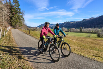 Obraz premium elderly couple rides electric mountain bikes on a trail in the Allgäu Alps near Oberstaufen in Bavaria. The scene depicts a wintry mountain landscape in early winter.
