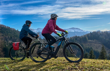 Fototapeta premium elderly couple rides electric mountain bikes on a trail in the Allgäu Alps near Oberstaufen in Bavaria. The scene depicts a wintry mountain landscape in early winter.