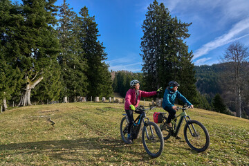 Naklejka premium elderly couple rides electric mountain bikes on a trail in the Allgäu Alps near Oberstaufen in Bavaria. The scene depicts a wintry mountain landscape in early winter.
