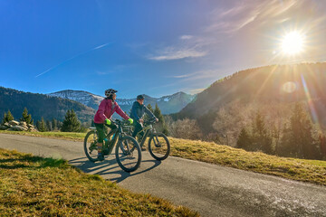 elderly couple rides electric mountain bikes on a trail in the Allg&auml;u Alps near Oberstaufen in Bavaria. The scene depicts a wintry mountain landscape in early winter.