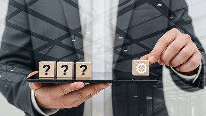 Businessman holds a tablet with question mark blocks and a gear block, seeking solutions.