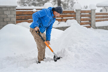 Man clearing snow from a driveway using a snow shovel. Winter sidewalks maintenance.