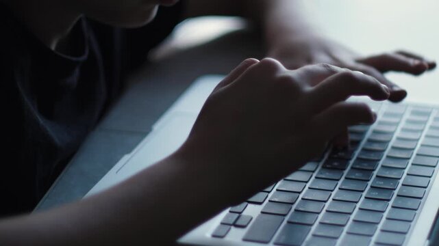 Close-up of child&rsquo;s hand pressing laptop keyboard keys, student learning on computer indoors
