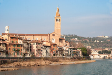 Obraz premium Picturesque view of Verona riverside with colorful houses, church tower and Ponte Pietra over the Adige River, capturing the historic charm of northern Italy.
