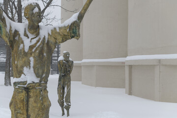 Obraz premium Apprensive Man, with defocused The Jubilant Man by Rowan Gillespie part of The Arrival, set beside the old Canada Malting silos on Eireann Quay, Toronto, during winter storm on 2026-01-15