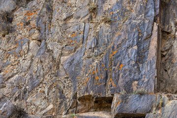Rugged rock face covered in vibrant lichen stands prominently in a mountainous region.