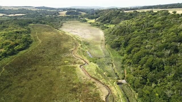 Drone footage showcasing Oxwich Marsh Nature Reserve on the Gower Peninsula in South Wales, revealing winding tidal channels, wetlands and surrounding farmland from above, filmed on a bright summer da