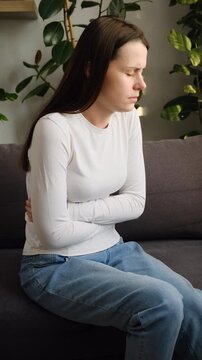 Sick woman in pain holding belly stomach feeling hurt abdomen ache gastritis pancreatitis symptoms. Sad female sit on couch suffering from indigestion flatulence abdominal problem