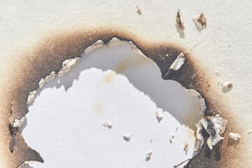 Burnt paper with irregular scorch marks on white surface demonstrating damage and texture.