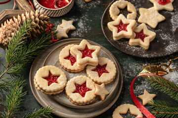 Fototapeta premium Homemade Linzer Christmas cookies filled with raspberry jam and dusted with sugar on ceramic plate with fir tree branches and festive decorations