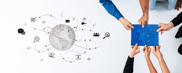 Diverse hands come together to solve a puzzle, symbolizing teamwork and global connectivity in a modern workspace filled with digital elements and visual communication. Trope