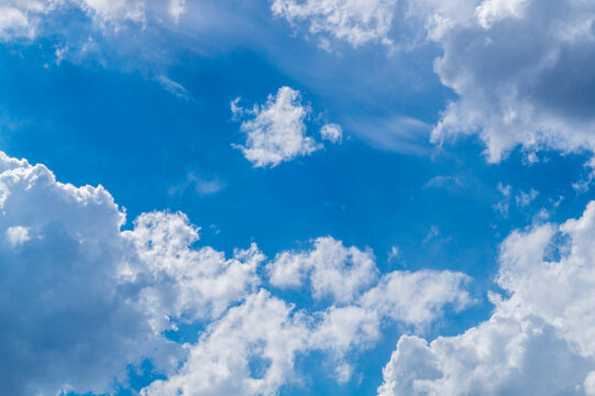 Photograph of airy white clouds against a blue sky, the edges of which are illuminated by lateral sunlight. Weather phenomena, synoptic forecasts. Blank for artworks