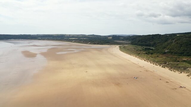 Drone footage capturing the sweeping sandy beach and turquoise waters of Oxwich Bay on the Gower Peninsula in South Wales, filmed on a bright summer day with clear skies and calm seas.