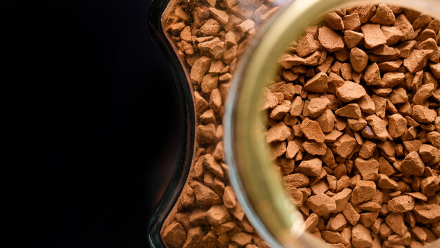 Macro close-up of soluble coffee grains in a glass container. Dry espresso powder texture for morning caffeine boost with place for text. Photo