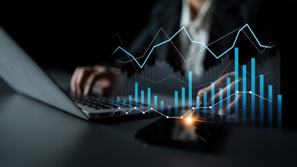 A professional analyzing financial data on a laptop while digital graphs and charts illuminate against a dark background, enhancing the office atmosphere. Scalp