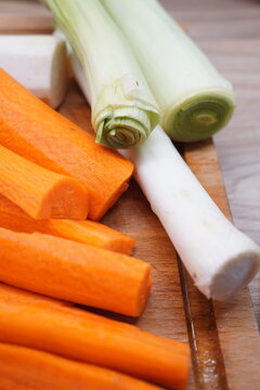 Freshly chopped carrots and leeks prepared for cooking on a wooden cutting board