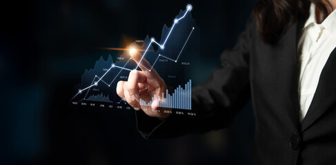 A businesswoman in a professional suit interacts with a modern digital graph showing stock market trends and growth, symbolizing finance and analysis. Scalp