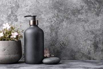 Matte black pump bottle and potted flowers against textured gray background