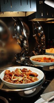 Delicious braised chicken and other Asian cuisine displayed in chafing dishes at a high-end restaurant buffet, ready for guests to enjoy. Vertical.