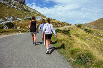 Family walking along a mountain road at Sedlo Pass in Durmitor, Montenegro, surrounded by alpine landscapes, capturing summer hiking, togetherness, and active outdoor travel in nature.